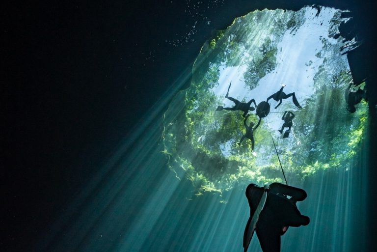 freediver at depth in the cenotes with other divers at the surface