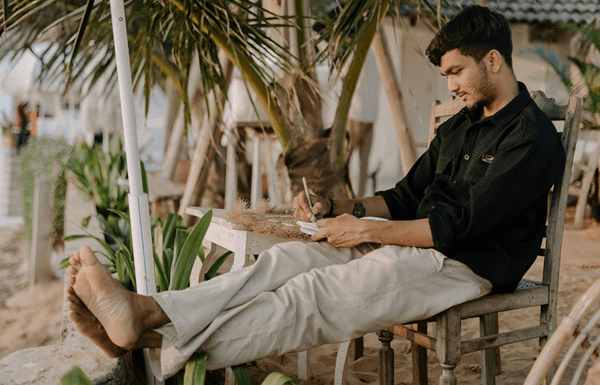guy sitting at beach writing in notebook